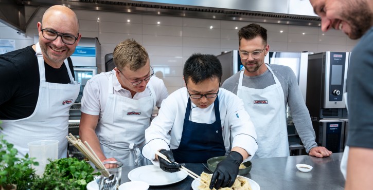 Chef plating dumplings with team in front of RATIONAL iCombi Pro combi ovens during a cooking workshop.