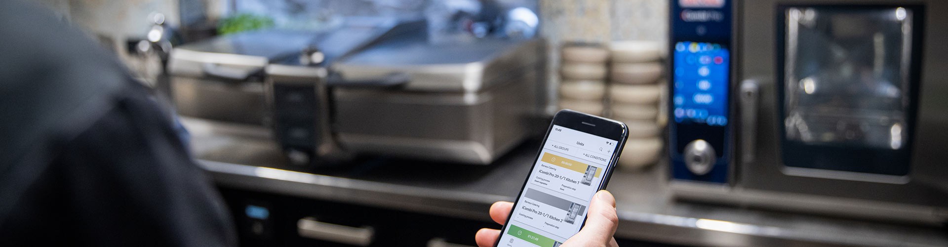One person is holding a smartphone on which ConnectedCooking can be seen. In the background an iCombi Pro and an iVario XS.