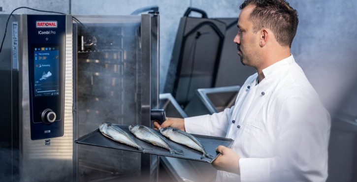 Chef wearing a white jacket puts a tray of fish into a steaming RATIONAL iCombi Pro combi oven in a commercial kitchen.
