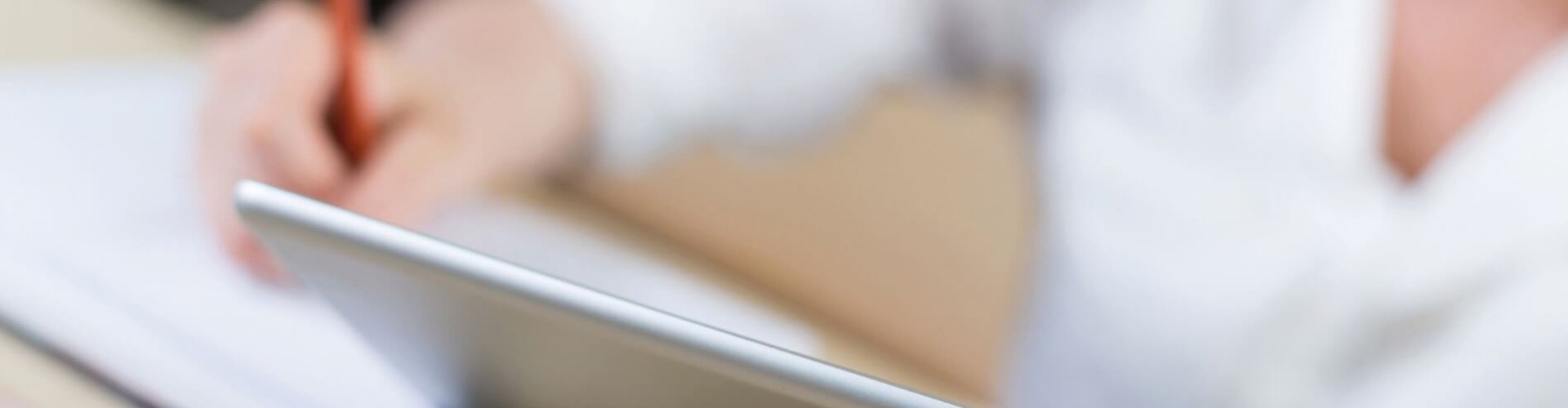 Persona con tablet che prende appunti con una matita su un blocco in un contesto di studio o lavoro.