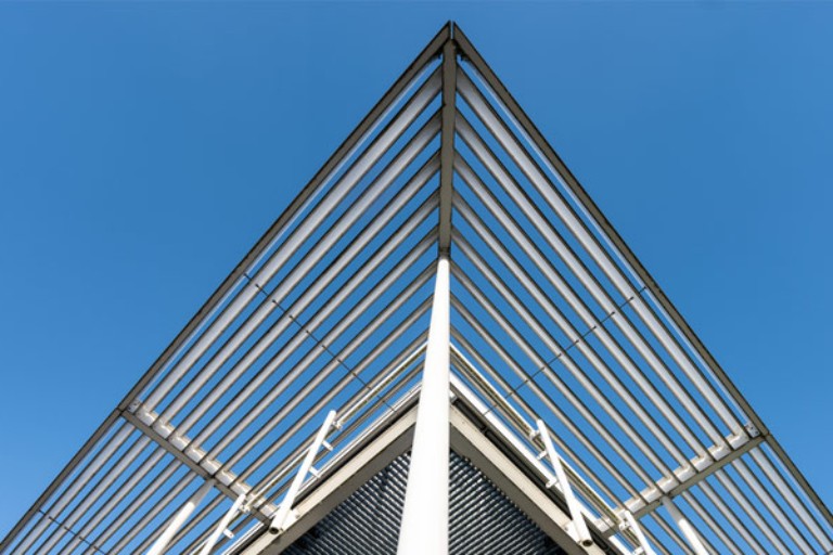 Modern architectural structure with steel beams forming a triangular roof against clear blue sky.