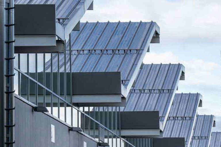 Modern industrial building with metal cladding and angular balconies under overhanging steel roofs.