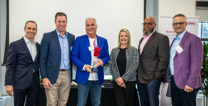 Six business professionals posing with an award trophy at a corporate recognition event.