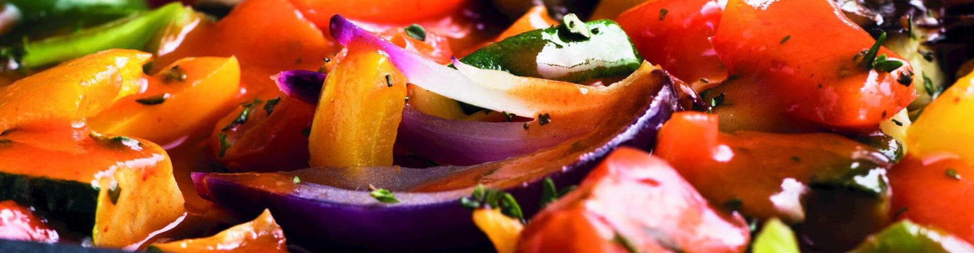 A close-up of a colorful ratatouille dish featuring a mix of bell peppers, zucchini, and onions, glistening with sauce.