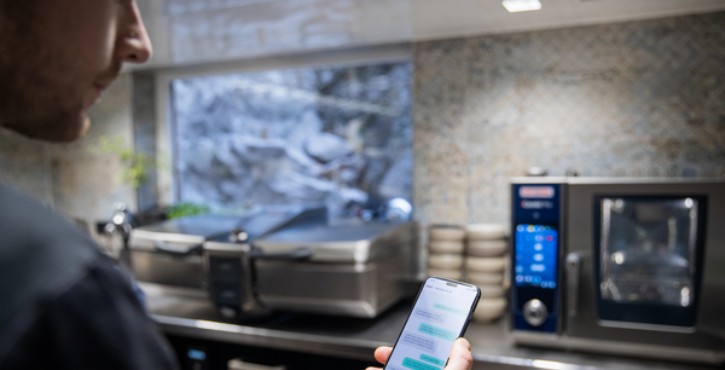 Chef consultant des messages sur son smartphone près d’un RATIONAL iCombi Pro four mixte.